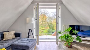 A modern loft apartment with a large window, a sofa, a television, and a potted plant. - Altstadt Apartments Verden - Andreasstraße (Verden)
