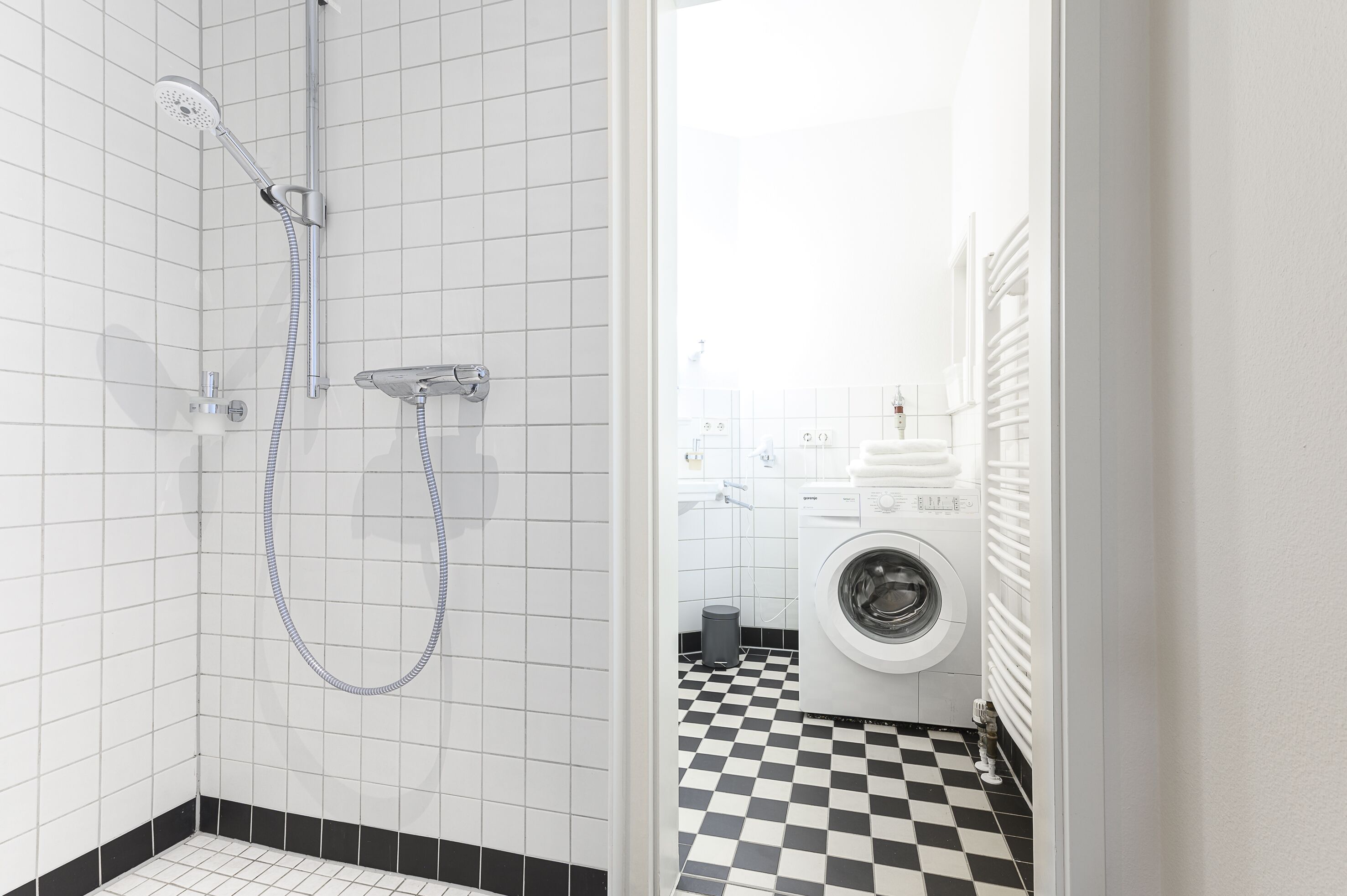 Un baño con ducha, lavadora y piso a cuadros.