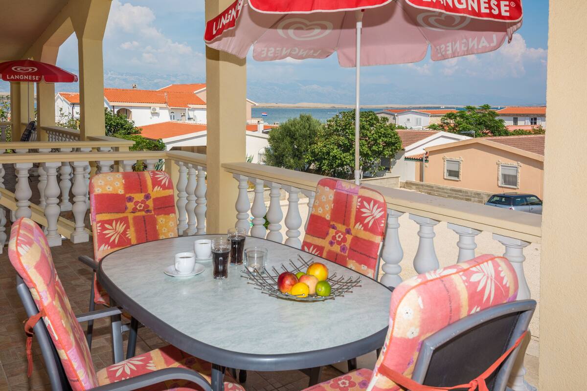 A balcony with a table, chairs, and a fruit bowl.