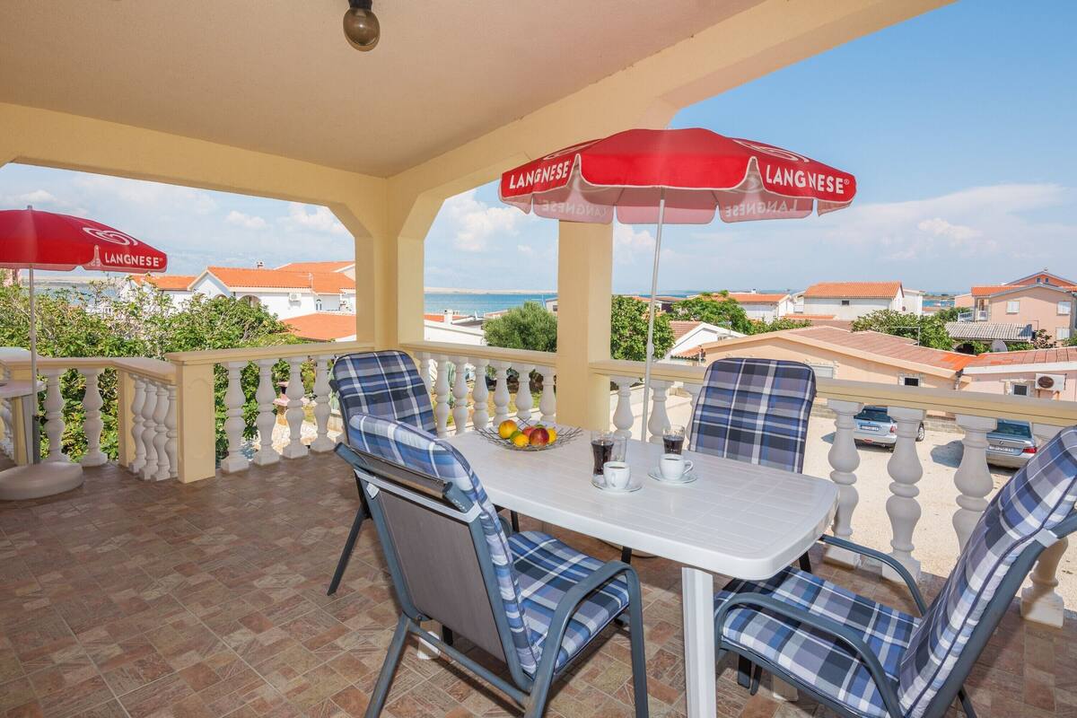A terrace with a table and chairs, red umbrellas, and a view of the sea and buildings.