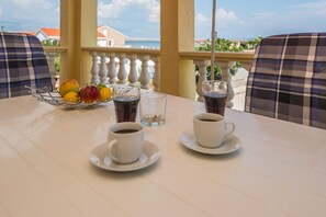 Et bord med to hvide kaffekopper, et glas vand og en frugtskål med æbler og citroner.