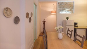 A dining area with a wooden table, chairs, a white pitcher with flowers, and a refrigerator. - Two-Bedroom Apartment (Porto)