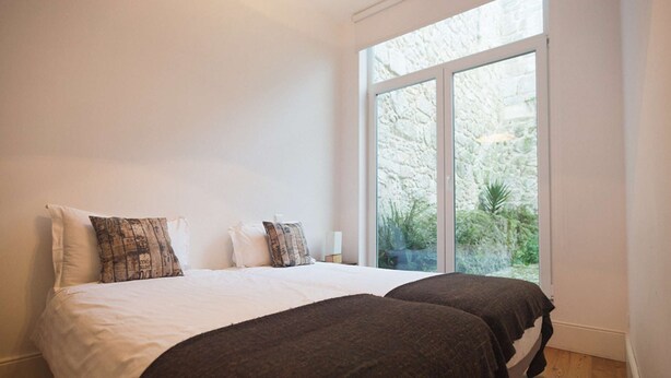 A bedroom with two beds, white bedding, and a large window with a view of greenery. - Two-Bedroom Apartment (Porto)
