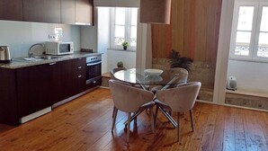 Una cocina moderna con armarios oscuros, un microondas y un lavamanos. Hay una zona de comedor con una mesa de vidrio y cuatro sillas.