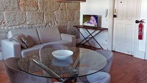 Una sala de estar moderna con una mesa de centro de vidrio, sillas tapizadas de color gris, una pared de piedra y una puerta blanca.