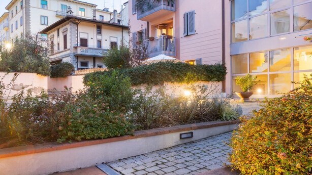 A multi-story building with balconies, a paved courtyard, and surrounding vegetation. - GuestHost - Comfortable 50sqm apartment with tiled patio that can accommodate up to 4 people. Located on the ground floor of a modern building of recent construction, the apartment is equipped with private parking space for a motorbike (inside the patio) (Firenze)