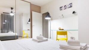 A modern hotel room with a bed, a desk, a chair, and a mirror. - GuestHost - Comfortable 50sqm apartment with tiled patio that can accommodate up to 4 people. Located on the ground floor of a modern building of recent construction, the apartment is equipped with private parking space for a motorbike (inside the patio) (Firenze)