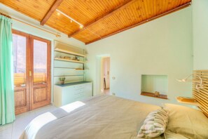 A bedroom with a wooden ceiling, a bed with a pillow, a desk with shelves, and a window with curtains.