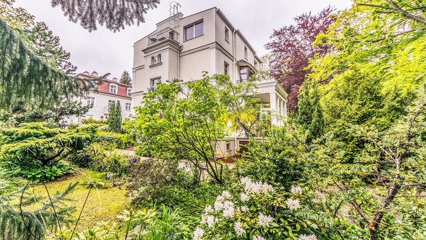 En moderne bygning med fladt tag, omgivet af frodigt grønt og blomstrende planter.