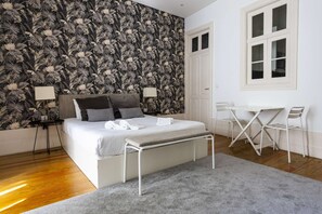 A bedroom with a bed, bedside lamps, a desk with chairs, and a window.