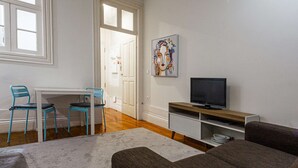 Un salon avec un téléviseur, deux fauteuils bleus, un canapé et un tableau accroché au mur.