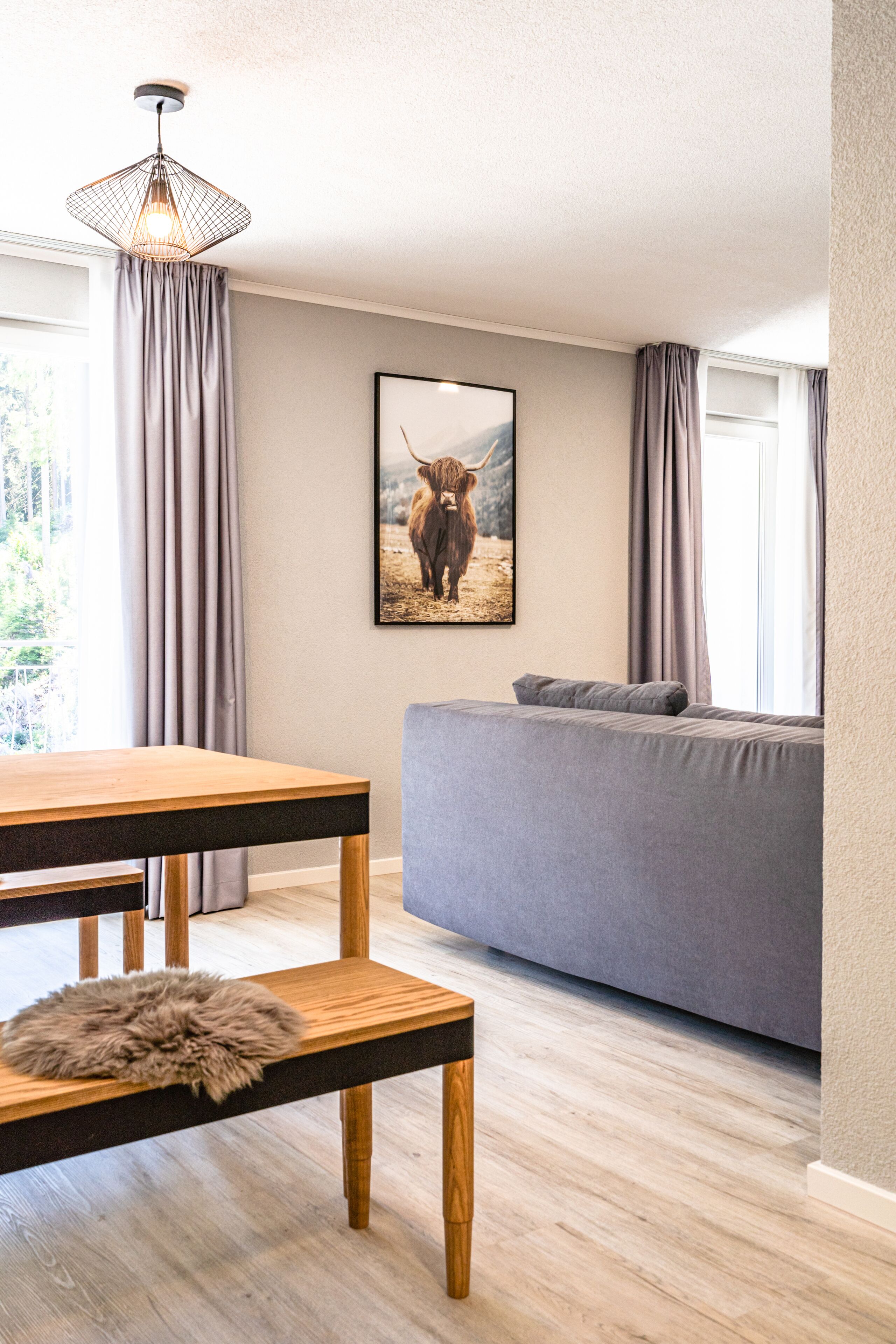 A modern living room with a wooden dining table, grey sofa, and a framed picture of a bull on the wall.