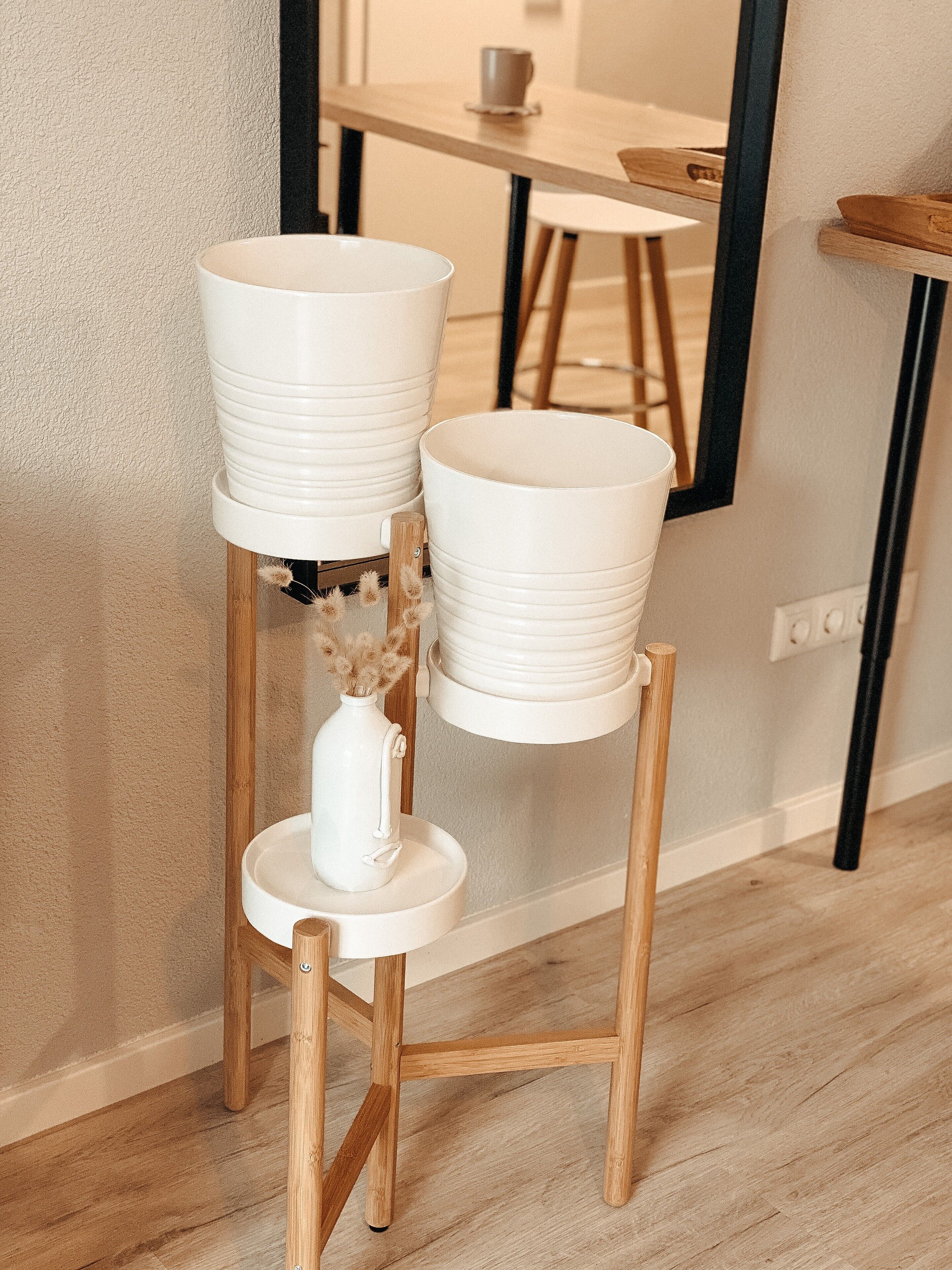 Un vaso in ceramica bianca su un supporto in legno, con un piccolo vaso contenente fiori secchi.