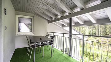 A balcony with a table and chairs, a window, and a view of trees.