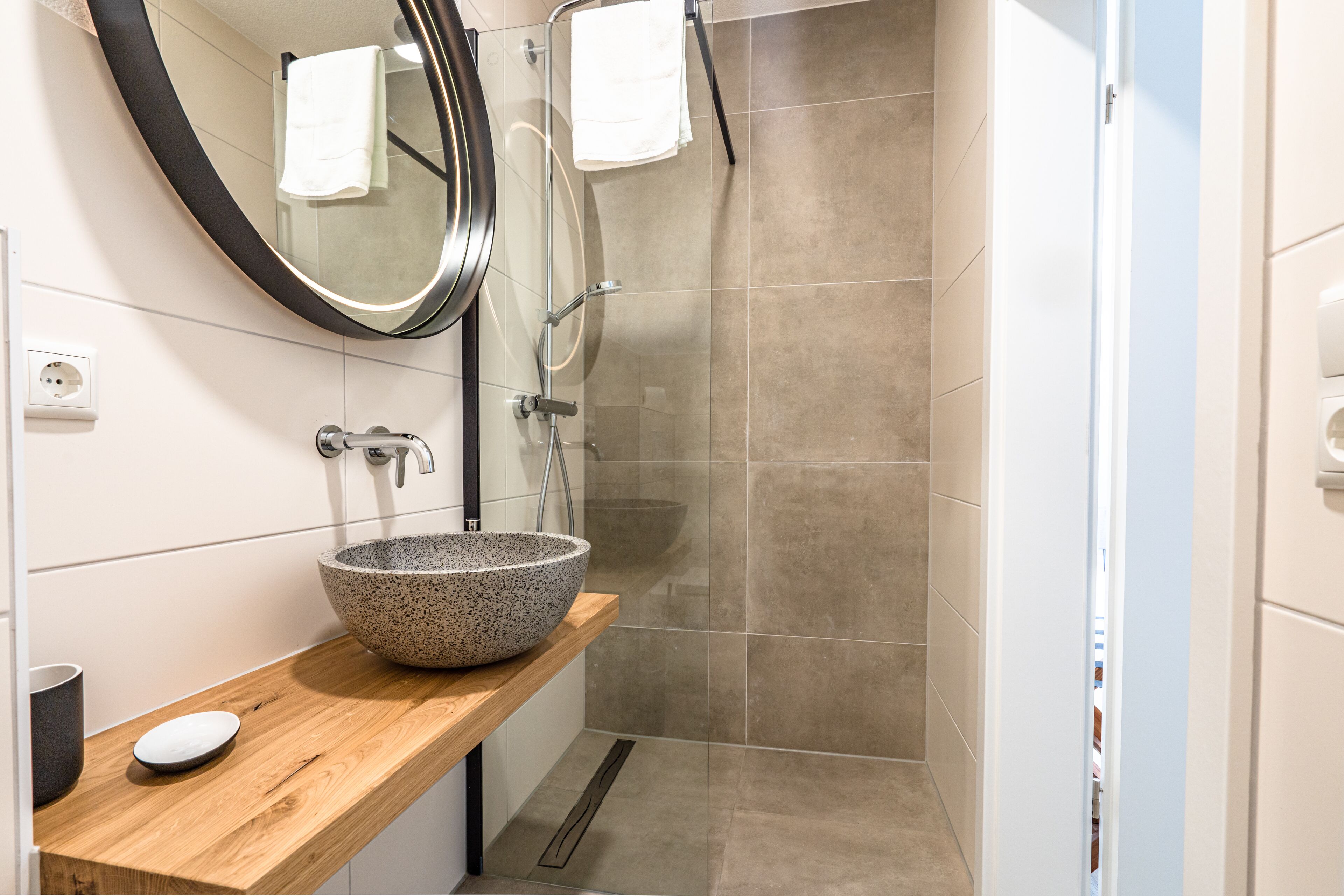 A modern bathroom with a freestanding sink, a large mirror, and a shower area.