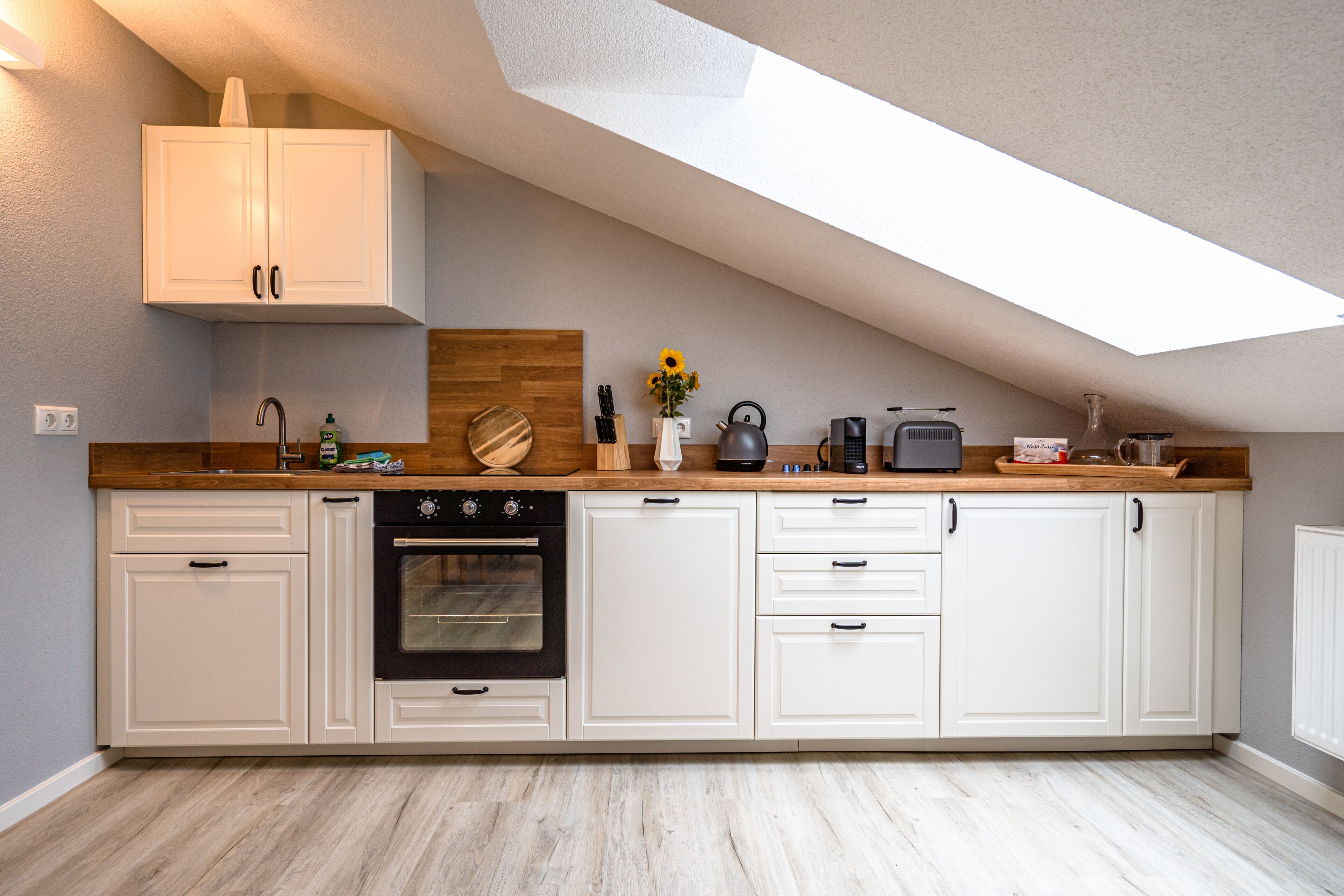 A modern kitchen with white cabinets, a wooden countertop, and a skylight.