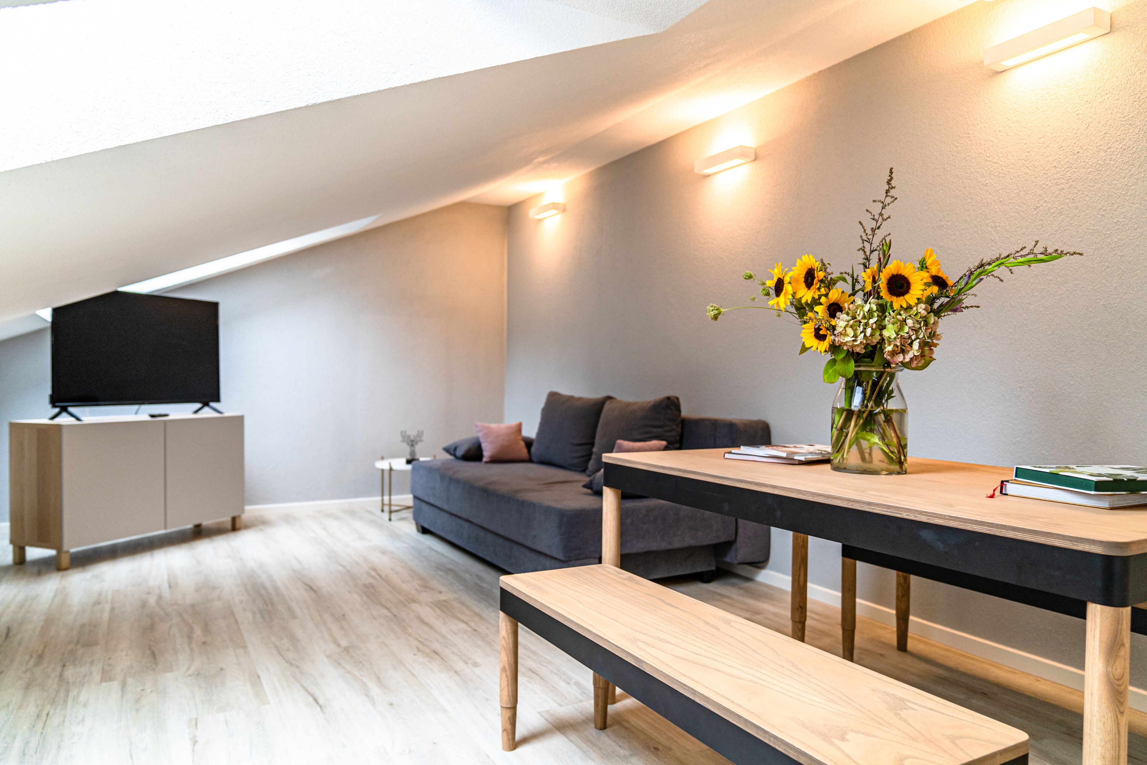 A modern living room with a sofa, a dining table, and a TV on a stand.