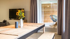 A modern living room with a long table, a flat-screen TV, a vase with flowers, and a window with blinds. - stuub langenbach (Titisee-Neustadt)