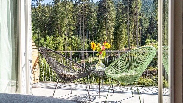 A balcony with two green chairs and a table, a vase with flowers, and a forest view. - stuub langenbach (Titisee-Neustadt)