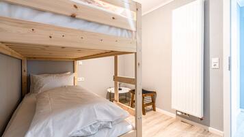 A bunk bed with white bedding, a small round table, and a chair in a room with wooden flooring and a white door.