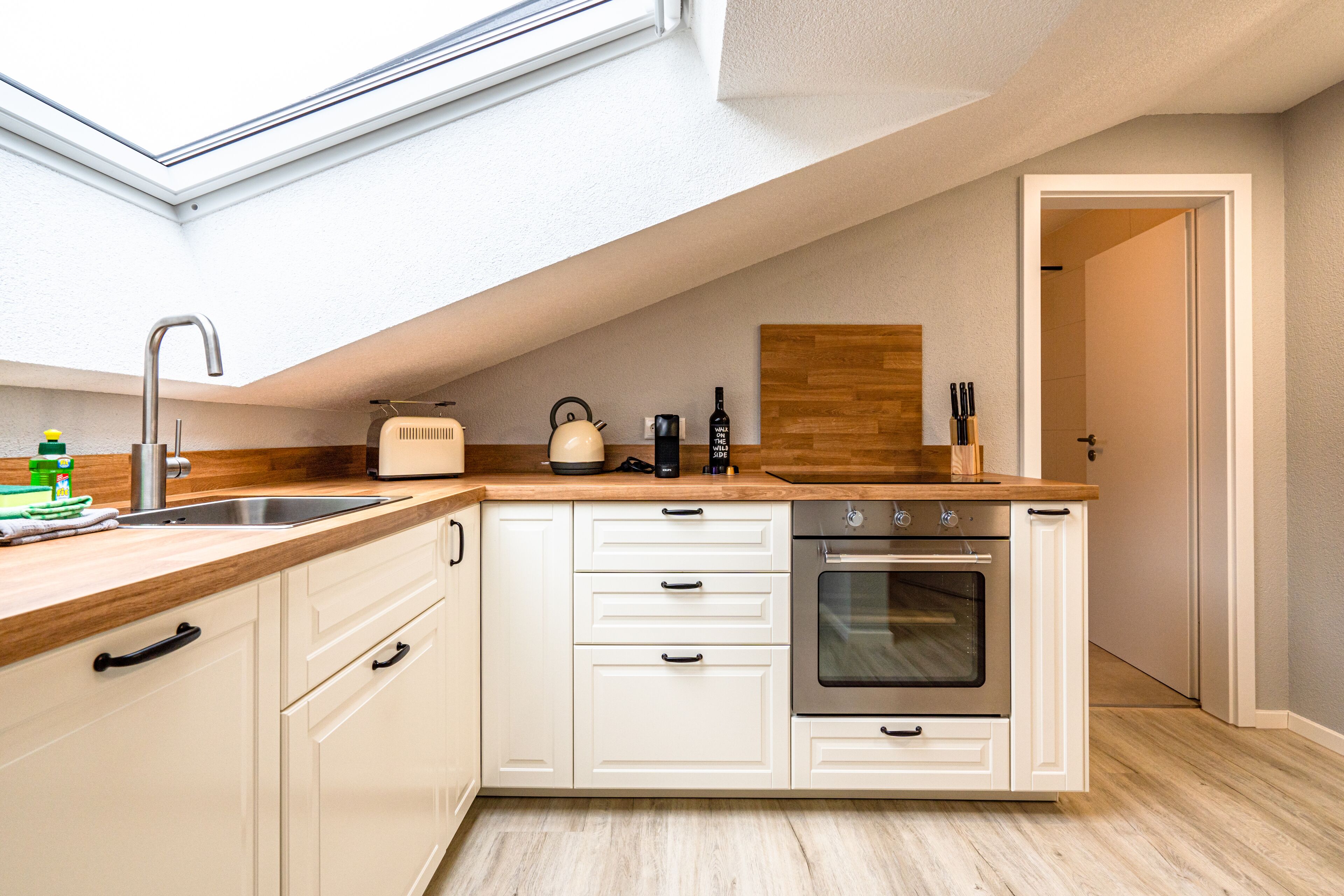 A modern kitchen with a skylight, wooden countertop, white cabinetry, and an oven.