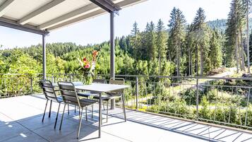 A covered outdoor patio with a table and chairs, overlooking a forested area.