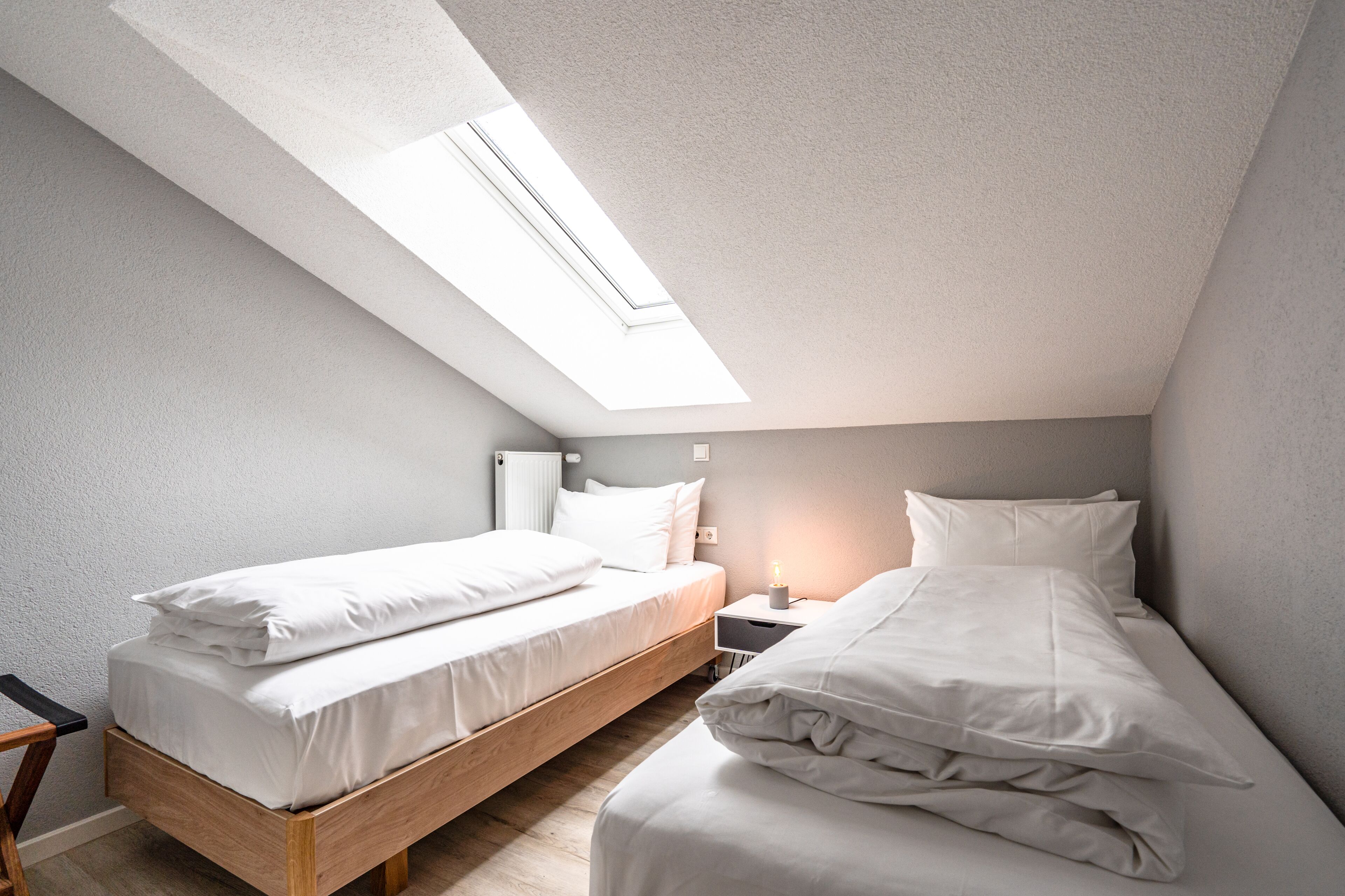 Een slaapkamer met dakraam, twee bedden, een nachtkastje en een stoel.