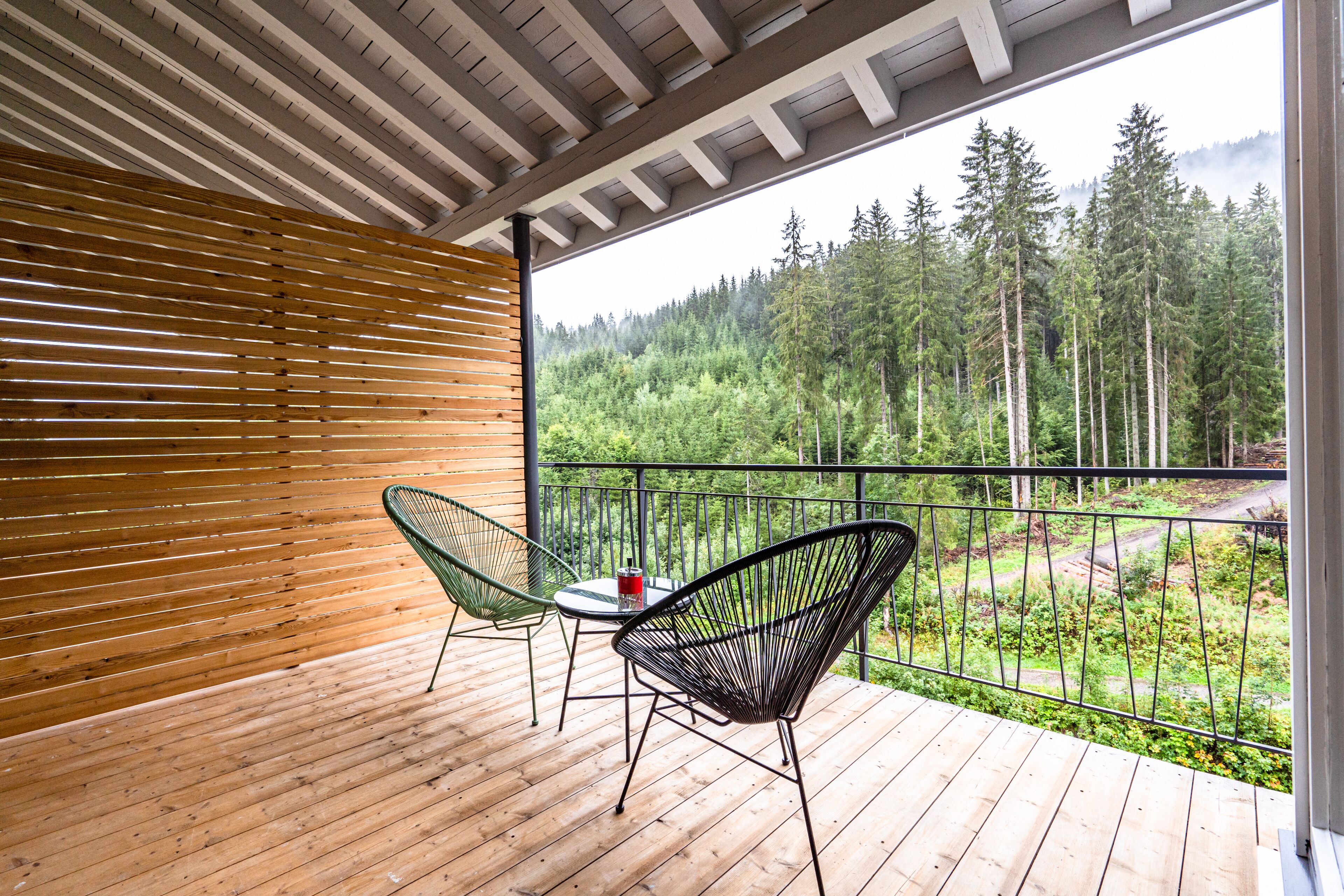 Una terraza de madera con dos sillas y una mesa, con vista a una zona boscosa.