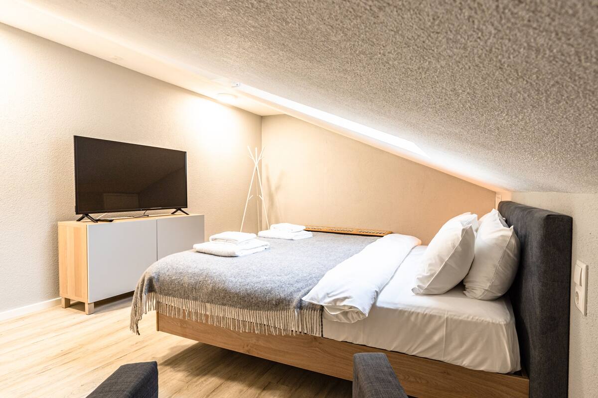 Ein modernes Schlafzimmer mit einem Bett, einem Flachbildfernseher, einem Nachttisch und einer Bank.