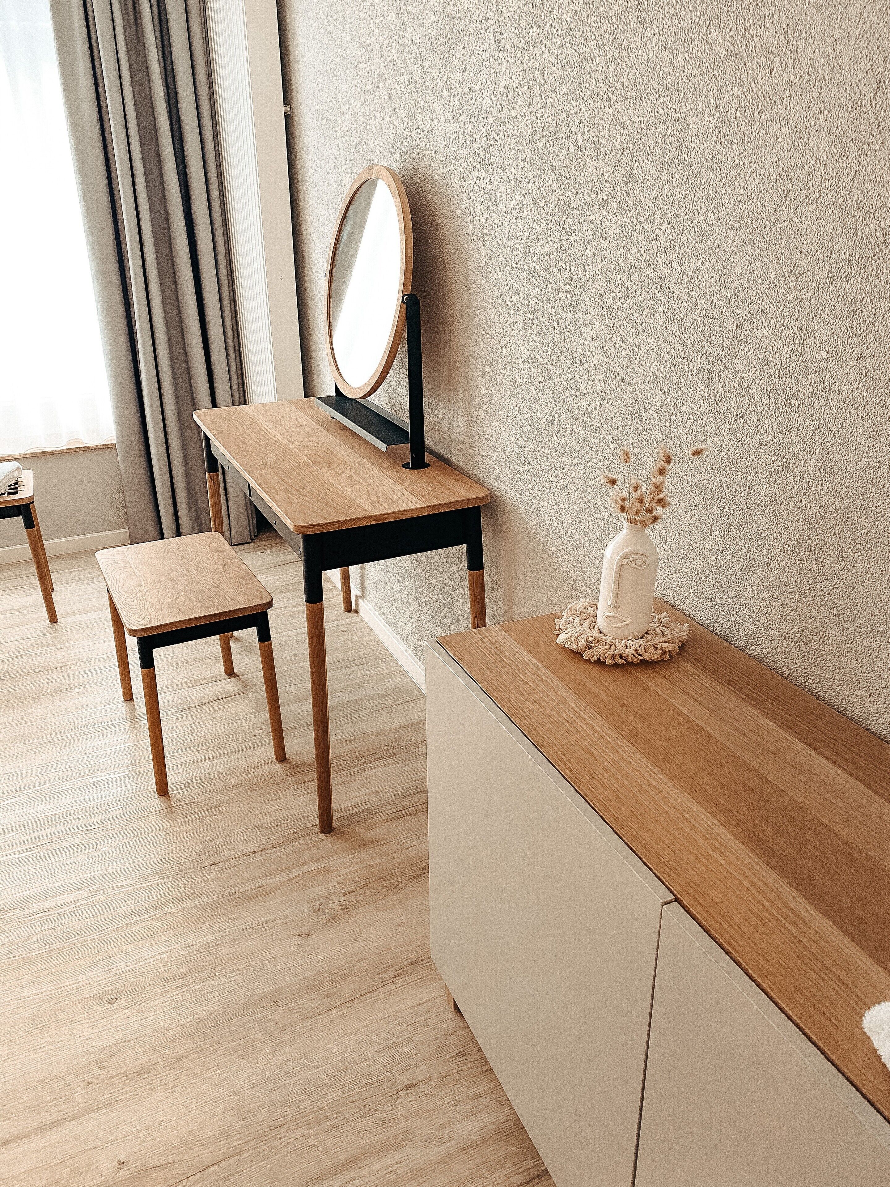 Una habitación minimalista con un escritorio de madera, un taburete pequeño y un jarrón decorativo sobre una mesa consola.