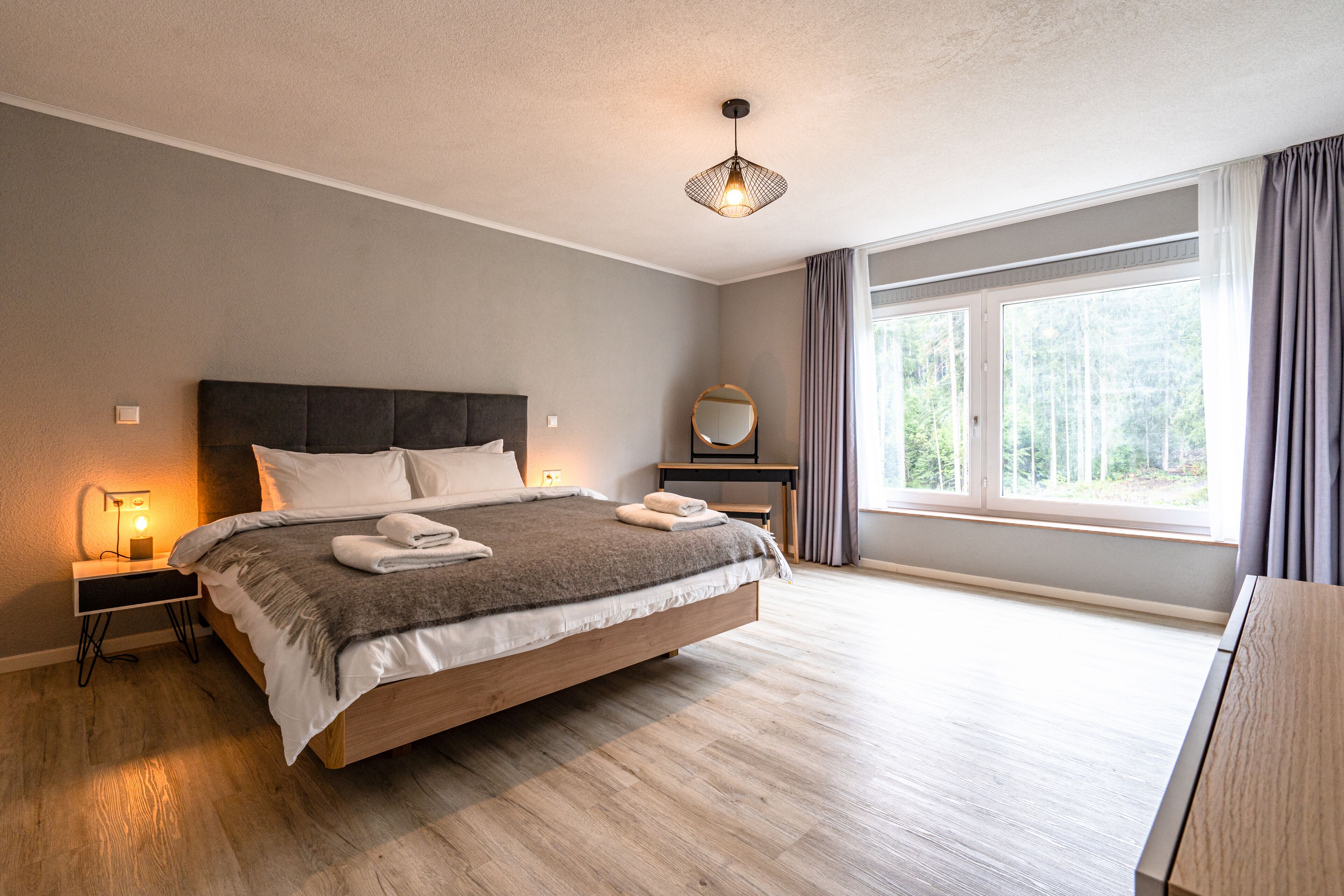 A modern bedroom with a large bed, bedside tables, a desk, and a window with curtains.