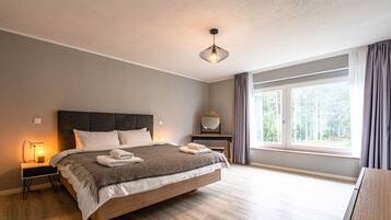 A modern bedroom with a large bed, bedside tables, a desk, and a window with curtains.