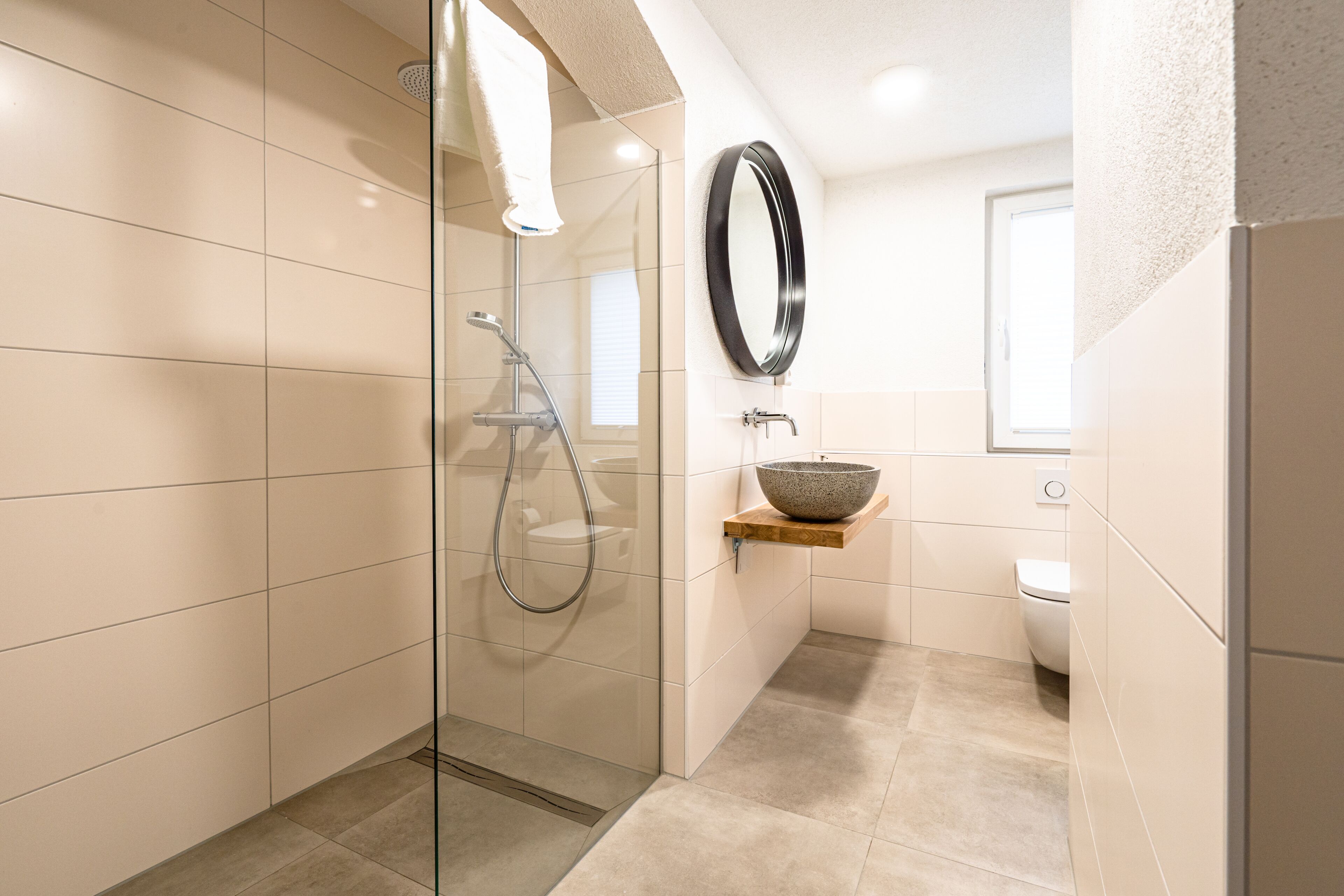 A modern bathroom with a glass-enclosed shower, a wooden shelf with a bowl, a toilet, and a mirror.