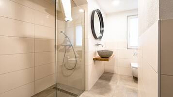 A modern bathroom with a glass-enclosed shower, a wooden shelf with a bowl, a toilet, and a mirror.