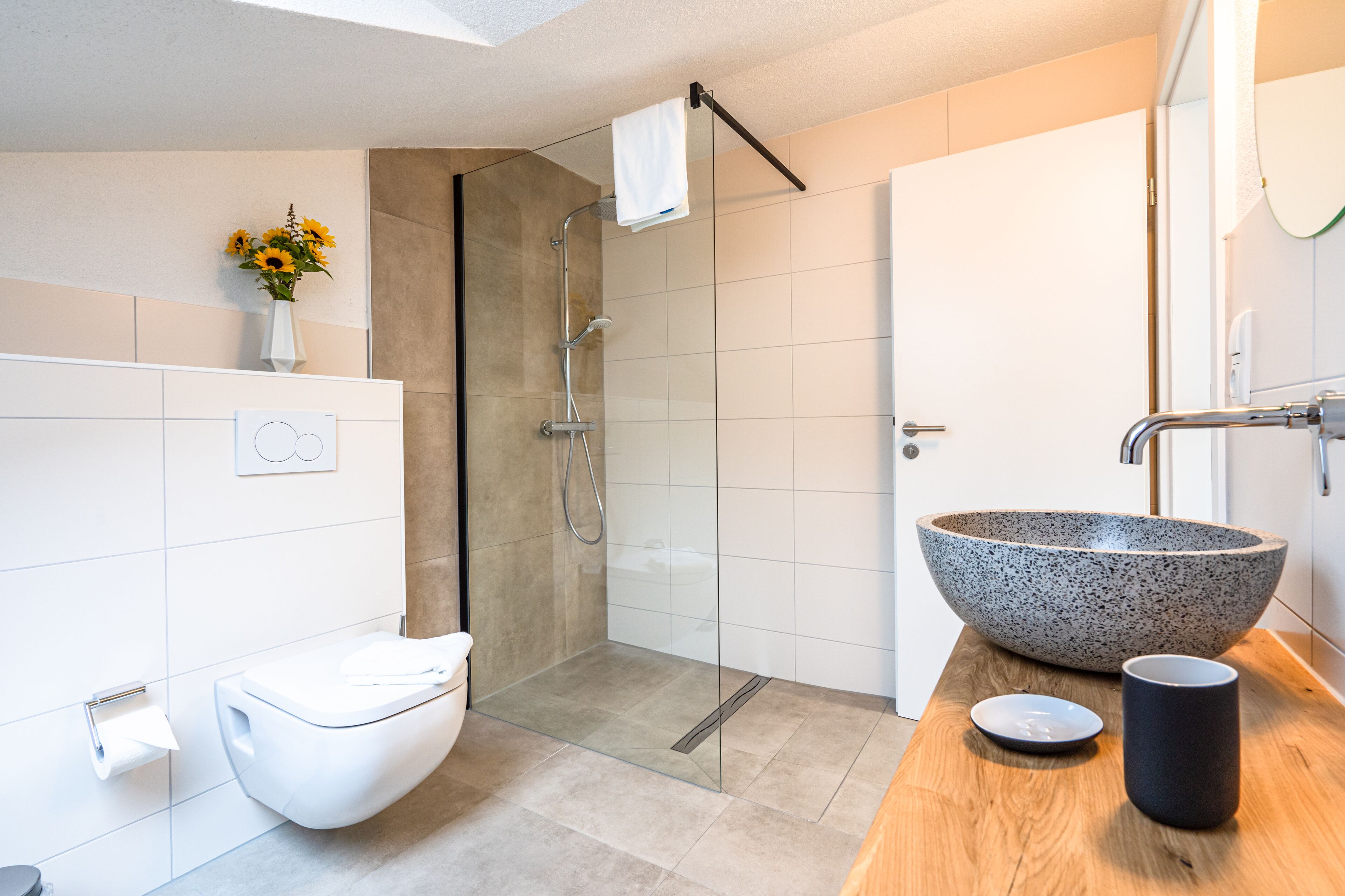 Een moderne badkamer met een douchecabine van glas, een wit toilet, een ruime stenen wasbak en een houten aanrechtblad.