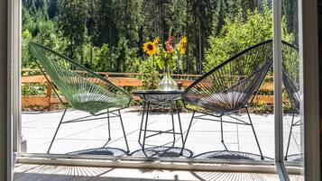A patio with two green wire mesh chairs, a small round table, and a vase with flowers.