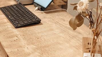 Un escritorio de madera con un teclado, una computadora portátil y un florero con flores secas.
