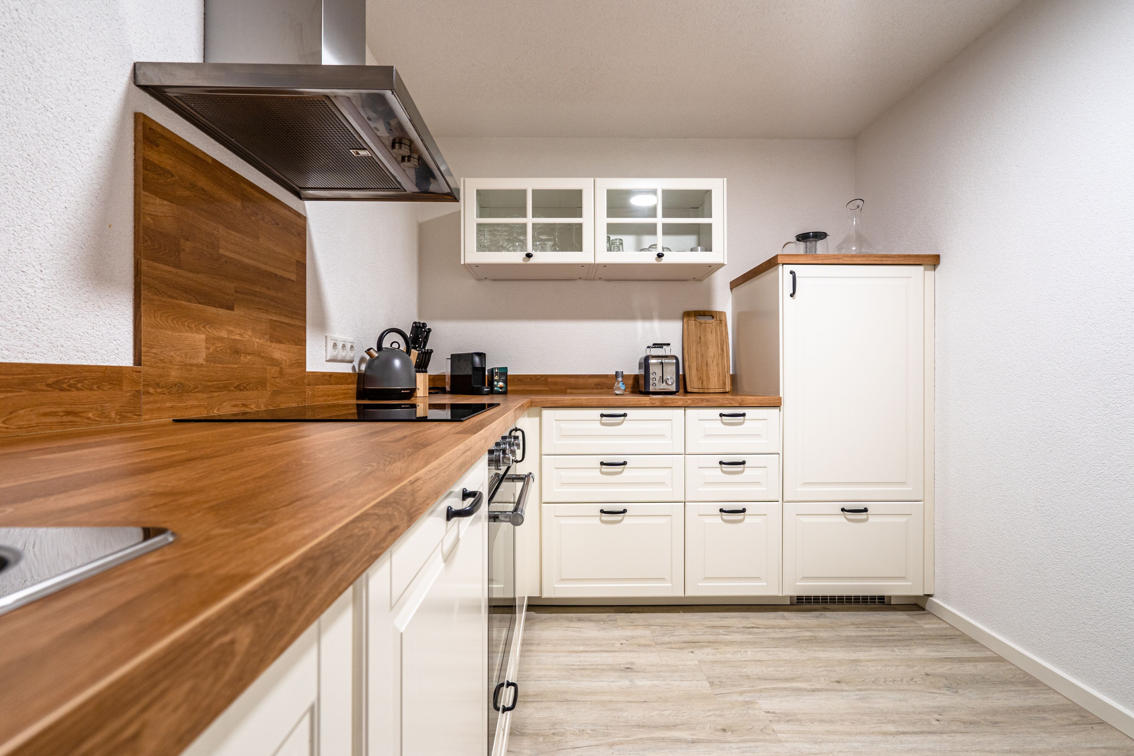 Una cocina con encimeras de madera, armarios blancos, una campana extractora de acero inoxidable y una ventana sobre los armarios.