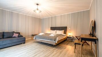 A modern bedroom with a wooden floor, a bed with a grey and white duvet, a grey sofa, a wooden nightstand, and a desk with a chair.