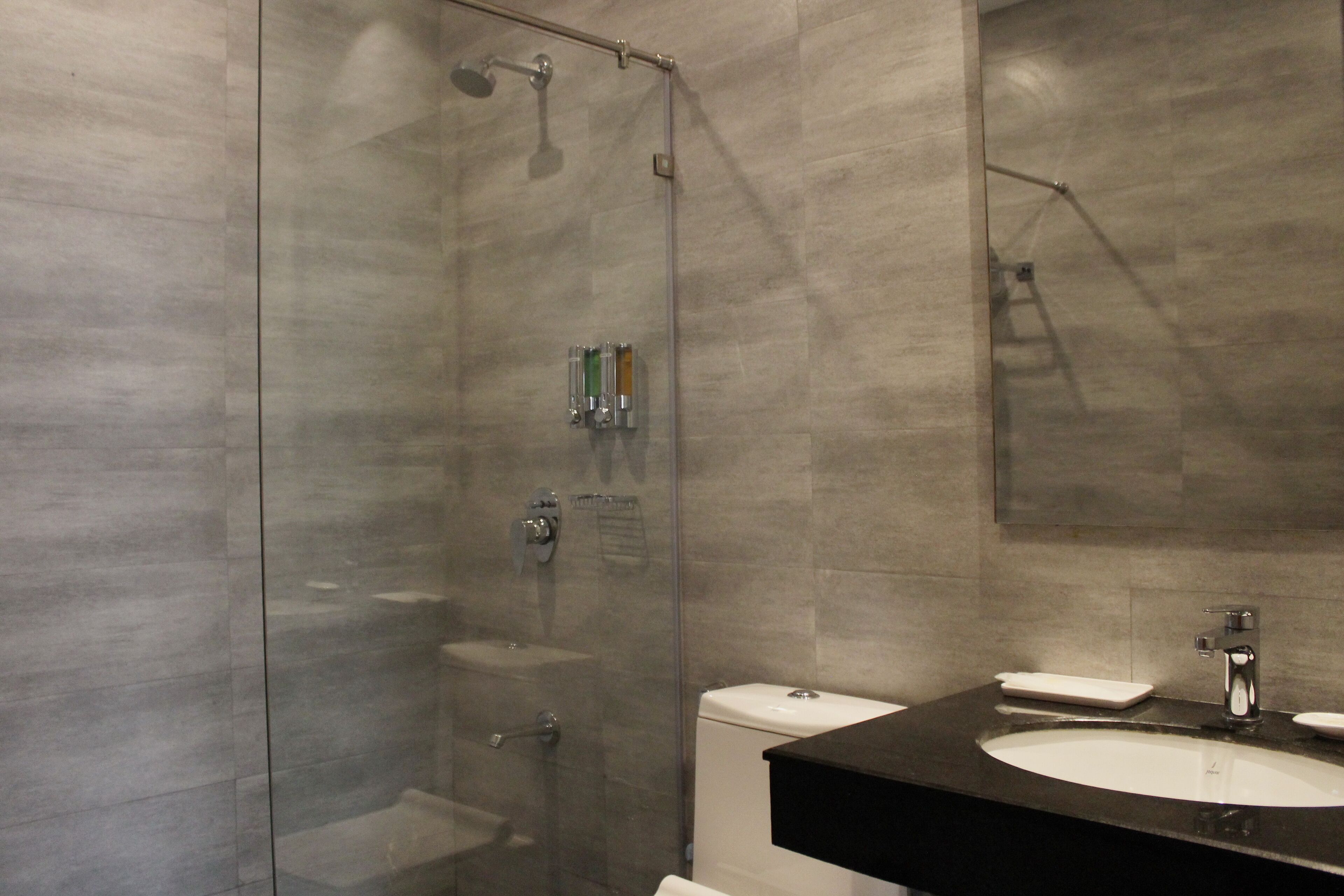 Une salle de bain moderne avec une douche à parois de verre, un lavabo sur un plan de toilette noir et des toilettes.