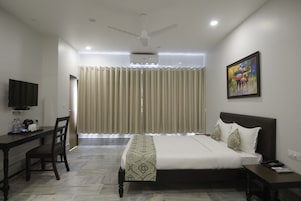 A hotel room with a bed, bedside table, desk, chair, and a television.