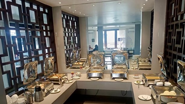 A buffet setup with multiple serving stations, including trays of food and various utensils. - Central Hotel (Phuntsholing)