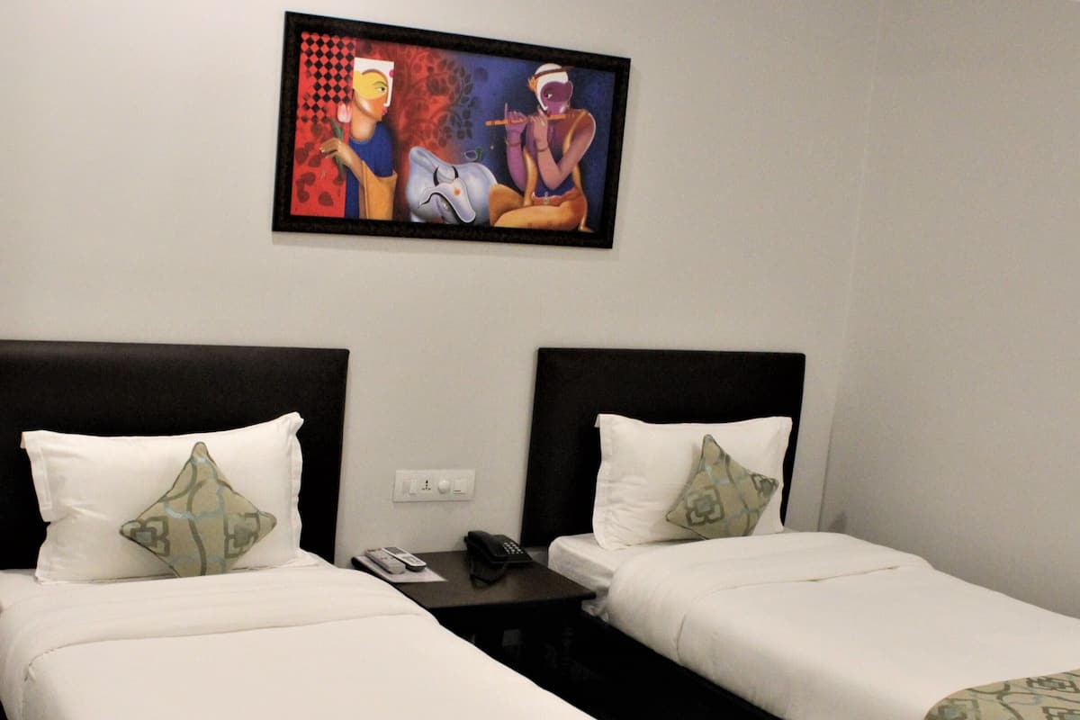 A hotel room with two single beds, a small table, a phone, and a painting on the wall.