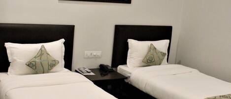 A hotel room with two single beds, a small table, a phone, and a painting on the wall.