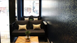 A dark-colored sofa with cushions, a wooden table with a vase, and a patterned wall. - Central Hotel (Phuntsholing)
