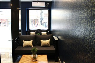 A dark-colored sofa with cushions, a wooden table with a vase, and a patterned wall.