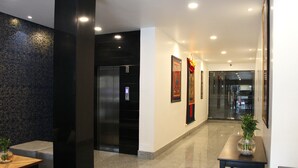 A modern lobby with a black elevator, a wooden bench, a glass table with a vase, and framed artwork on the walls. - Central Hotel (Phuntsholing)