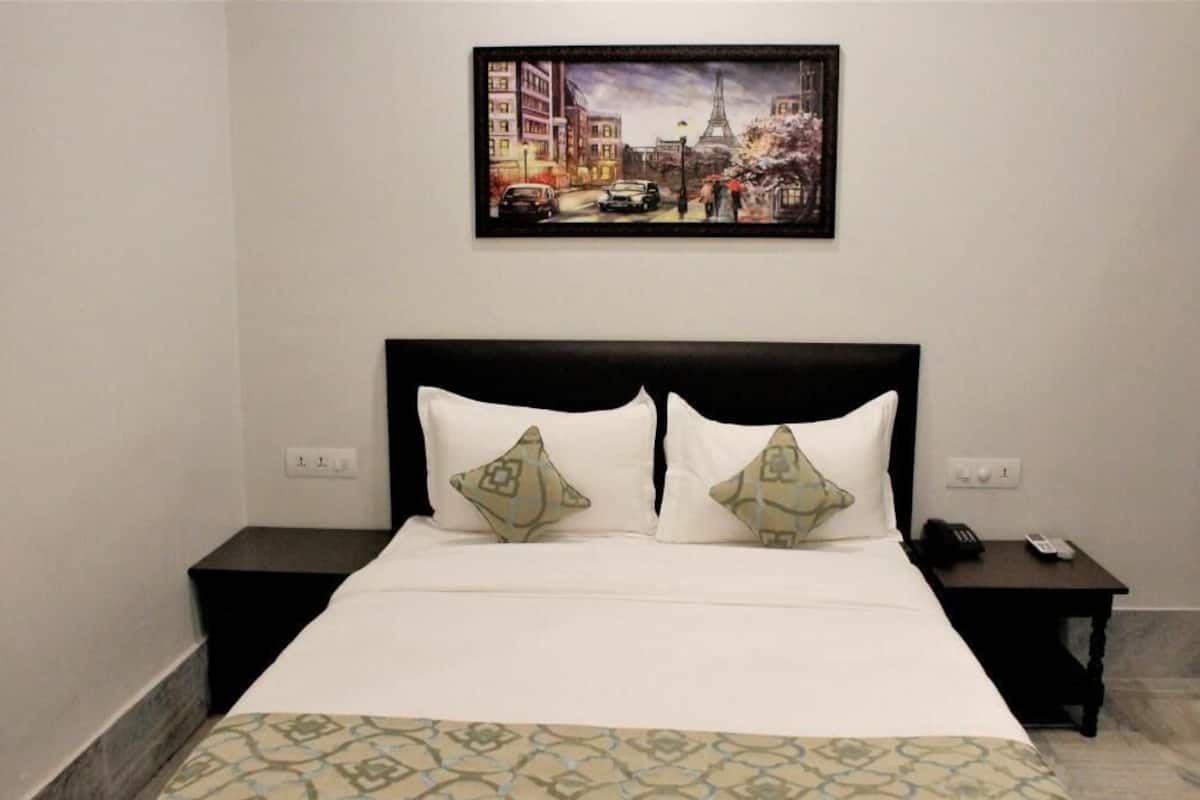 A hotel room with a bed, two bedside tables, a nightstand, and a painting of a cityscape.