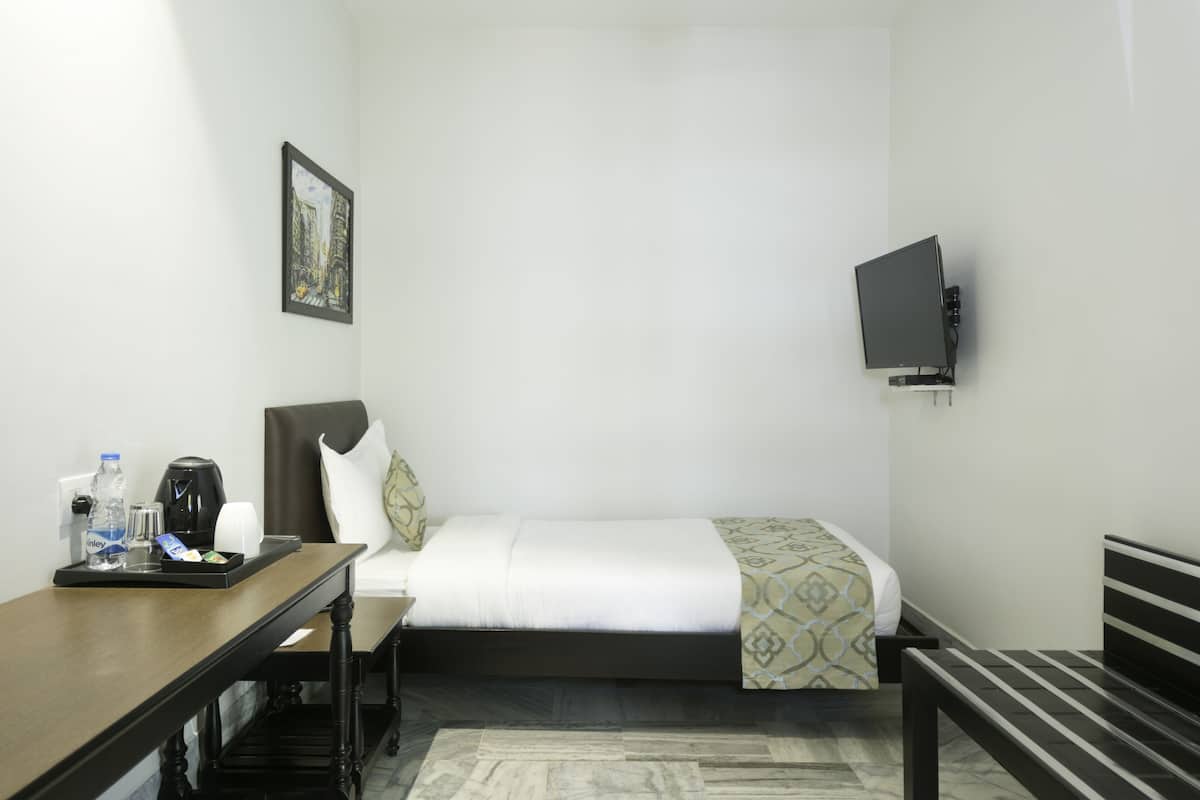 A hotel room with a bed, a desk with a tray of items, a chair, a television mounted on the wall, and a framed picture on the wall.