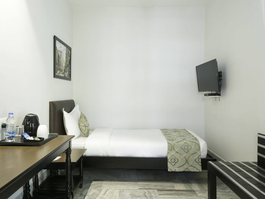 A hotel room with a bed, a desk with a tray of items, a chair, a television mounted on the wall, and a framed picture on the wall.